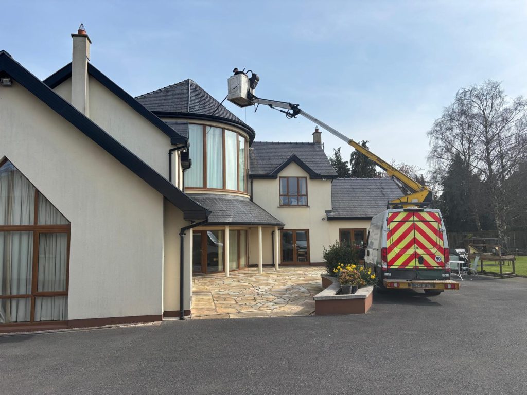 Brian Kelly Services mechanical hoist cleaning the roof and render of a large house